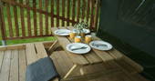 Wooden bench with dining plates set up outside of the Safari tent at Little Nook Glamping, Cornwall