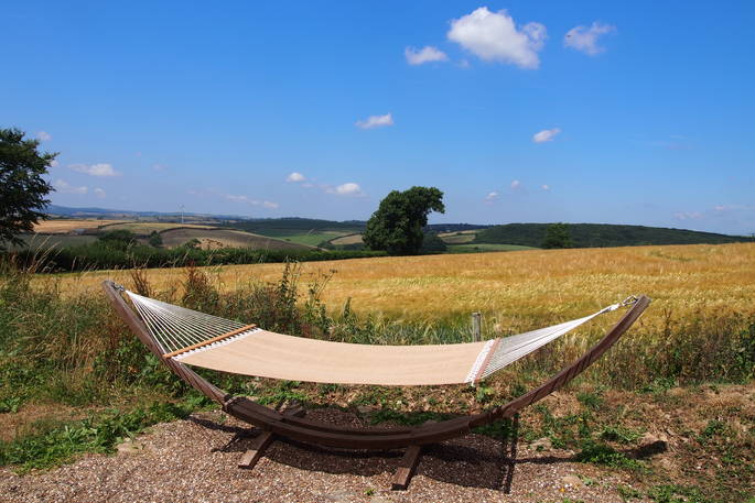 A comfy double hammock in the sun, overlooking the beautiful calm countryside with yellow and green fields, under a blue sky at Quiet of Stars in Cornwall