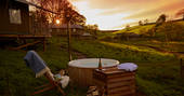 Sun setting in the sky with champagne bottle and glasses sitting next to Bovey safari tent wood-fired hot tub