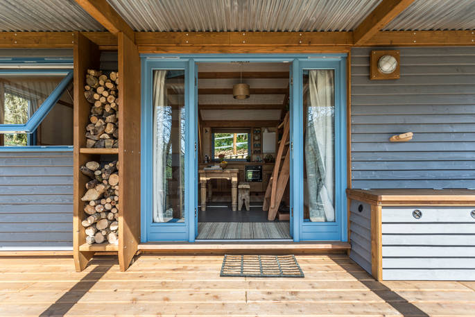 Doorway into Carpenter Cabin with store of firewood under covered veranda 