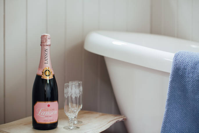 A bottle of bubbly and two glasses sit on a table by the bath in Sergeant Troy