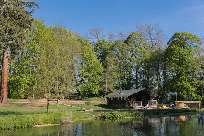 The Fisherman's Hideaway safari tent with hot tub and BBQ outside at The Lost Garden Retreat surrounded by a lake in Suffolk