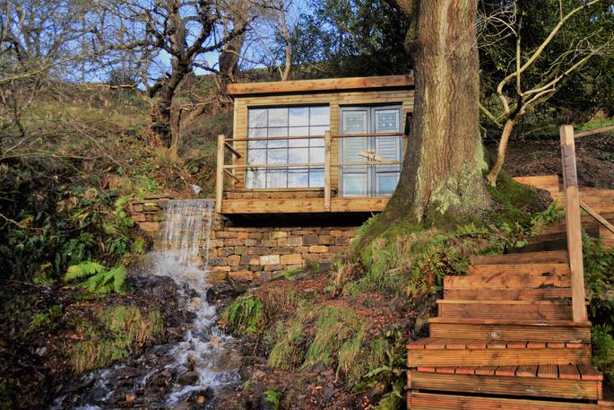 Water flowing underneath and windows wrapping right round a colourful cabin, Falling Water at Ponden MIll in Yorkshire 