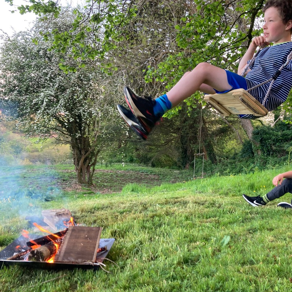 A boy on a tree swing seeming to go over a firepit