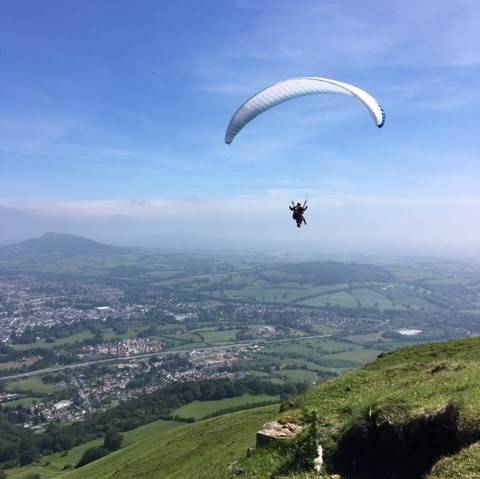 A paraglider hanging in the air above the Powys countryside